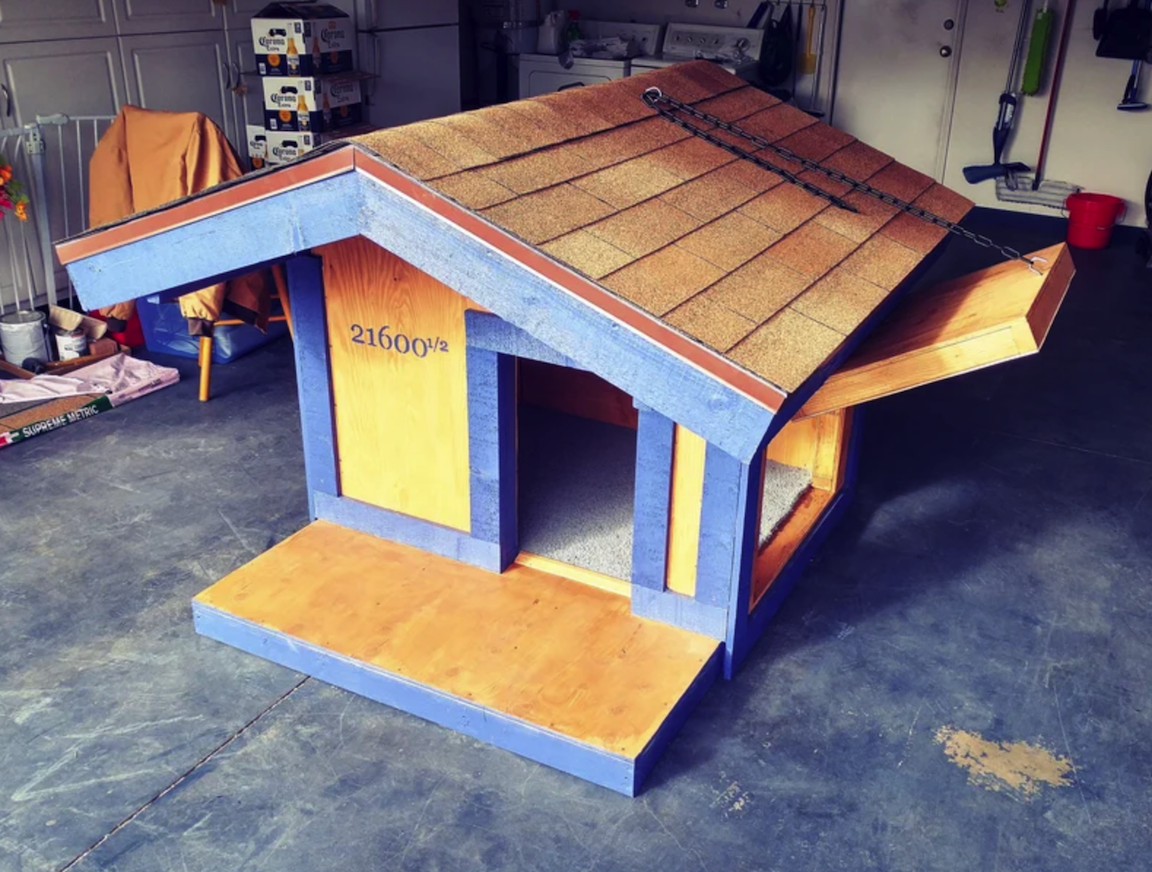 diy dog house inside garage with blue siding tiled roof and two doorways one with a doorway that opens upwards
