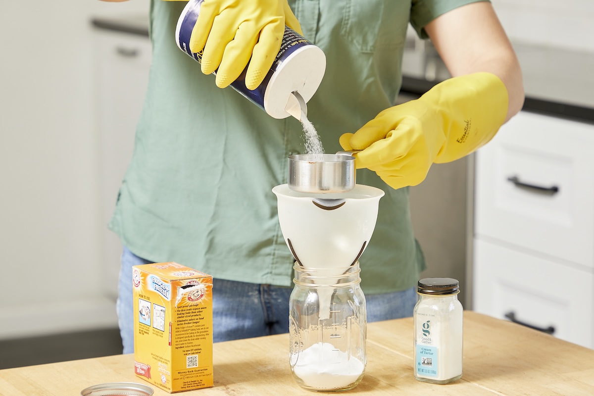 Woman pours salt from salt shaker through a funnel into a glass jar.