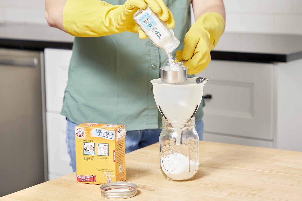 Woman pours cream of tartar through a funnel into a glass jar.