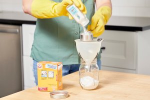 Woman pours cream of tartar through a funnel into a glass jar.