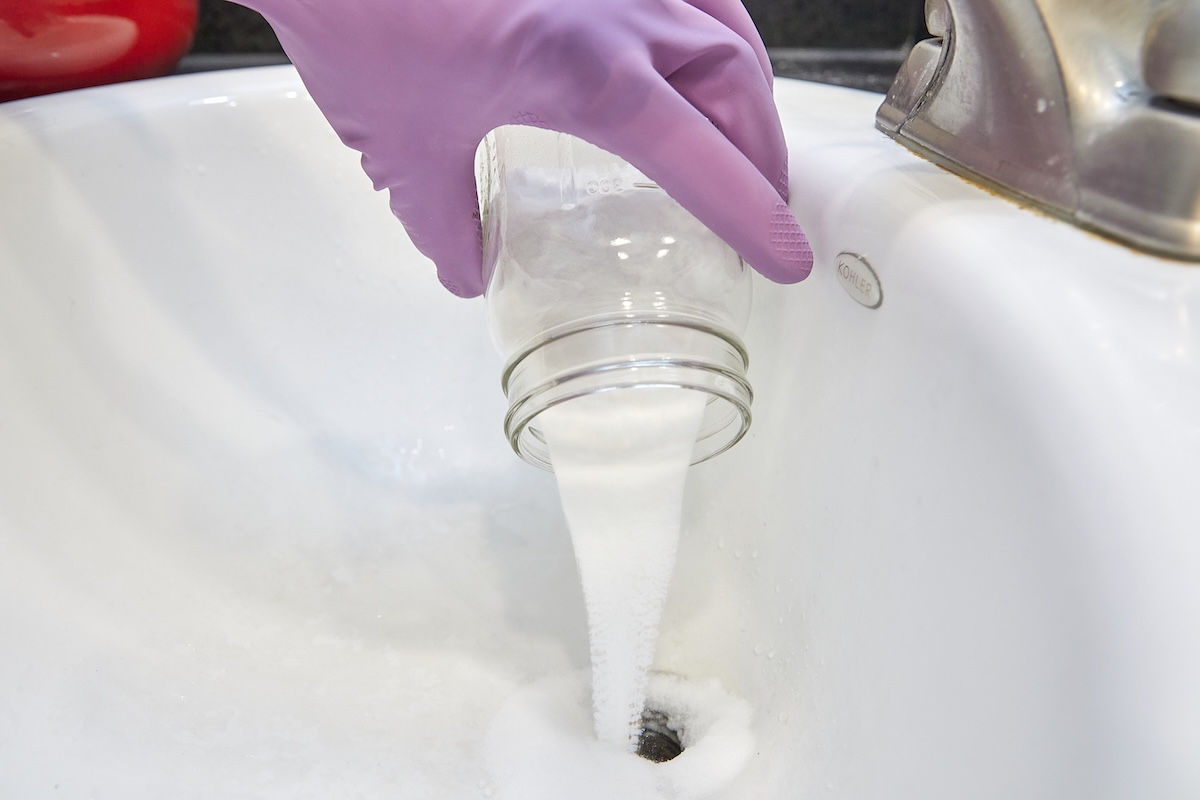 Person wearing rubber gloves pours homemade drain cleaner into sink drain.