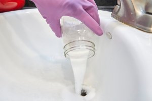 Person wearing rubber gloves pours homemade drain cleaner into sink drain.
