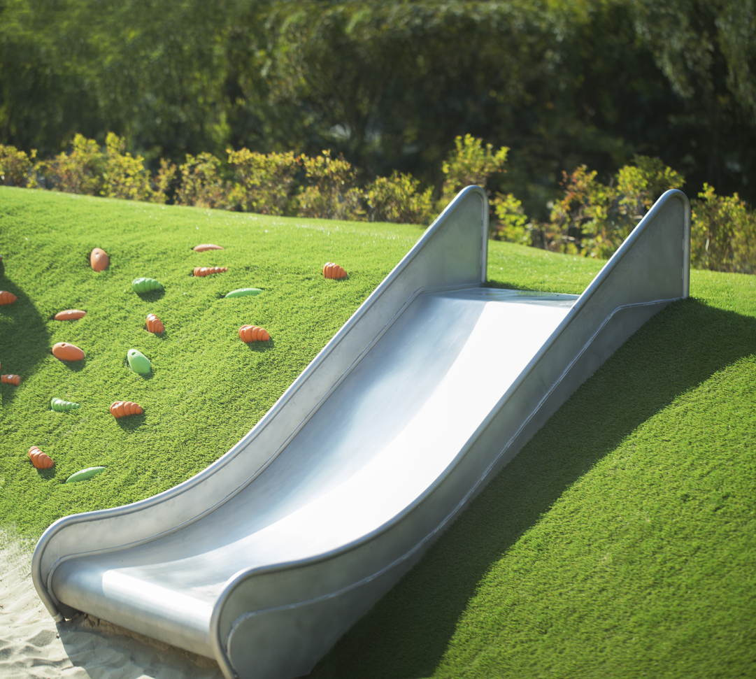 Hill overgrown with grass and metal slide at the playground in summer sunny day"n
