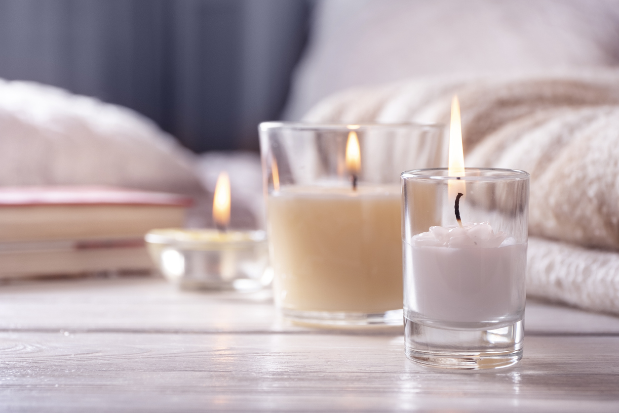 close up on three light colored candles with flames on light wood floor in front of blurry bed and books