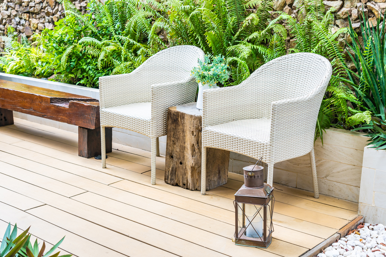 two white patio chairs on deck next to wood bench with ferns in landscaping behind them next to a rock path