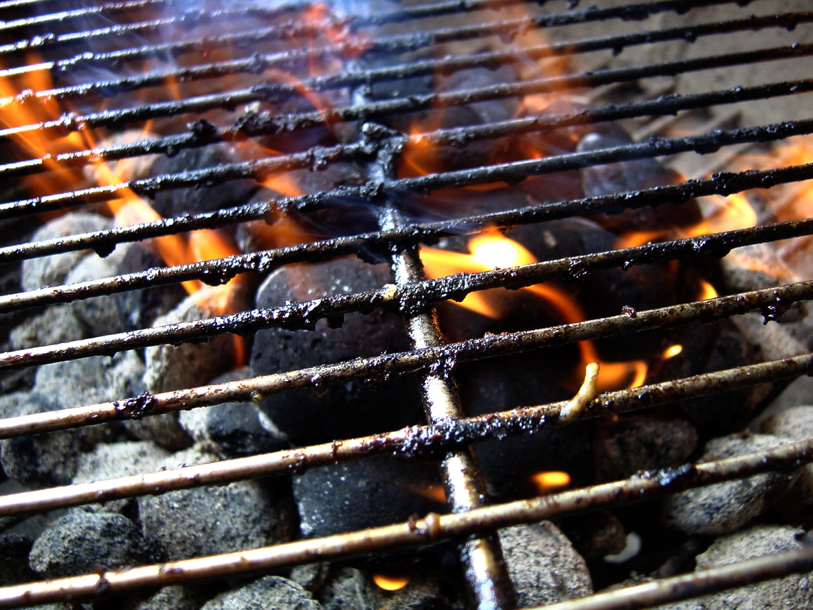 close up on grill covered in charred grease with flames and charcoal underneath