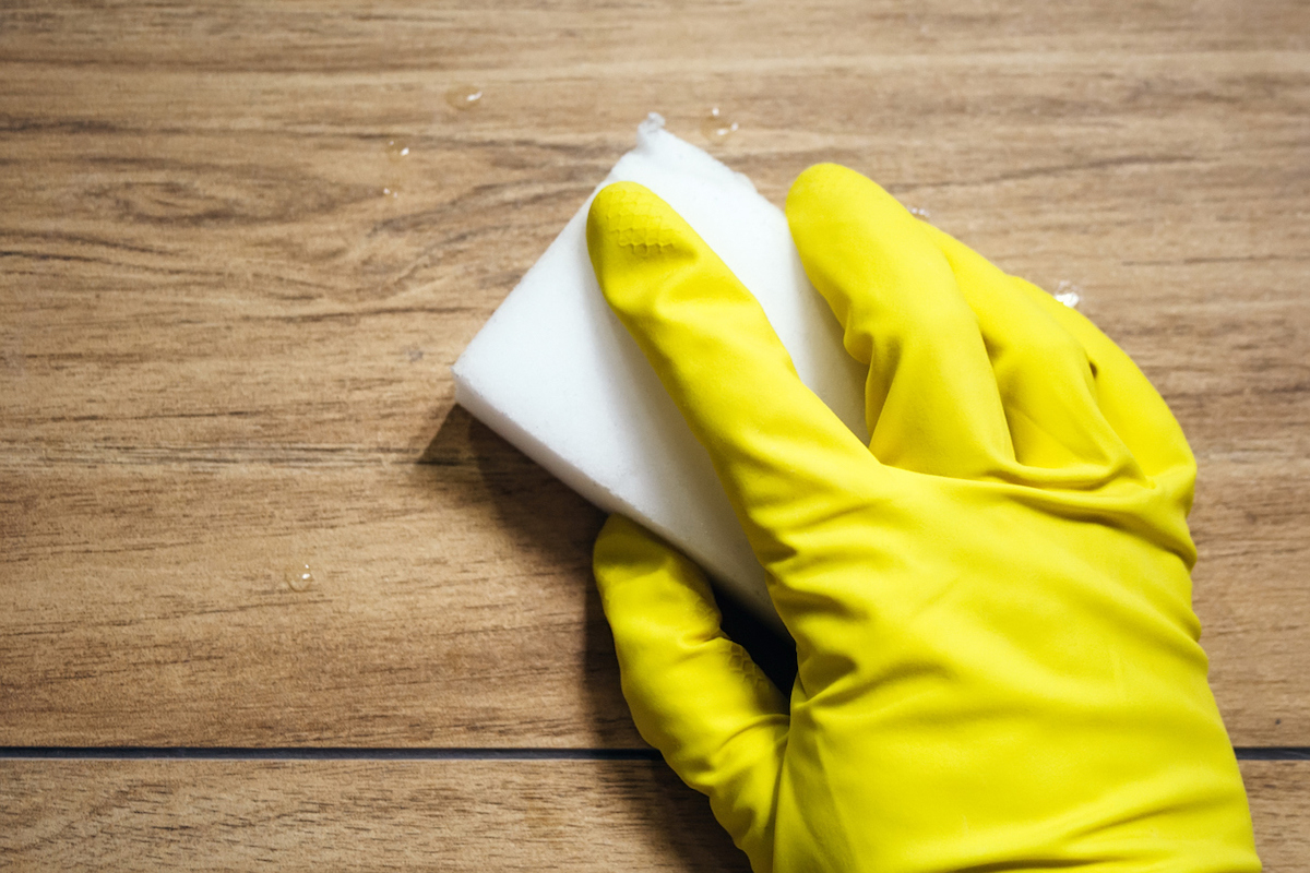 hand with rubber glove using a magic eraser to clean a wood look tile and grout