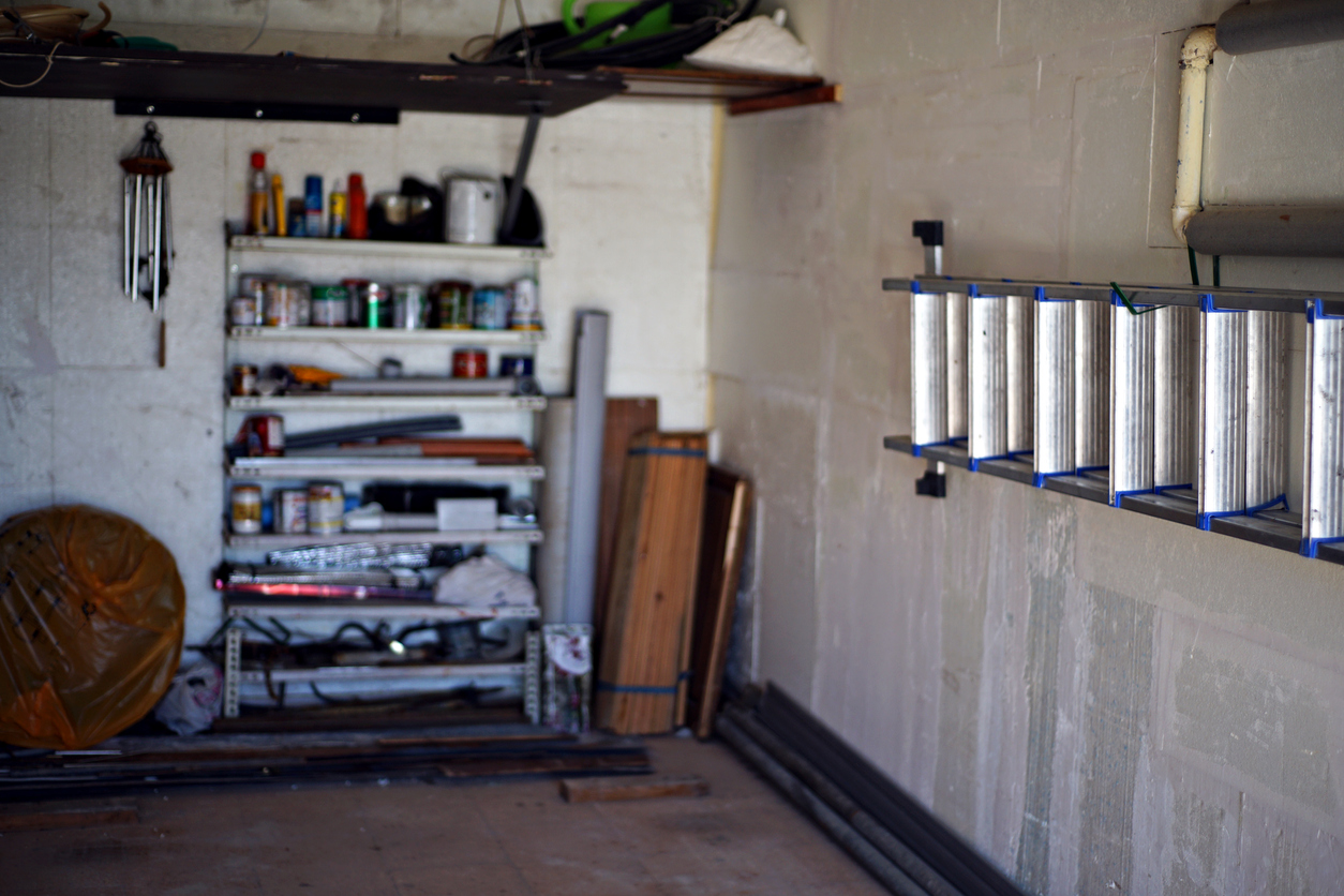 inside garage with white brick walls with ladder mounted to wall and a shelf in the back with paint cans in storage