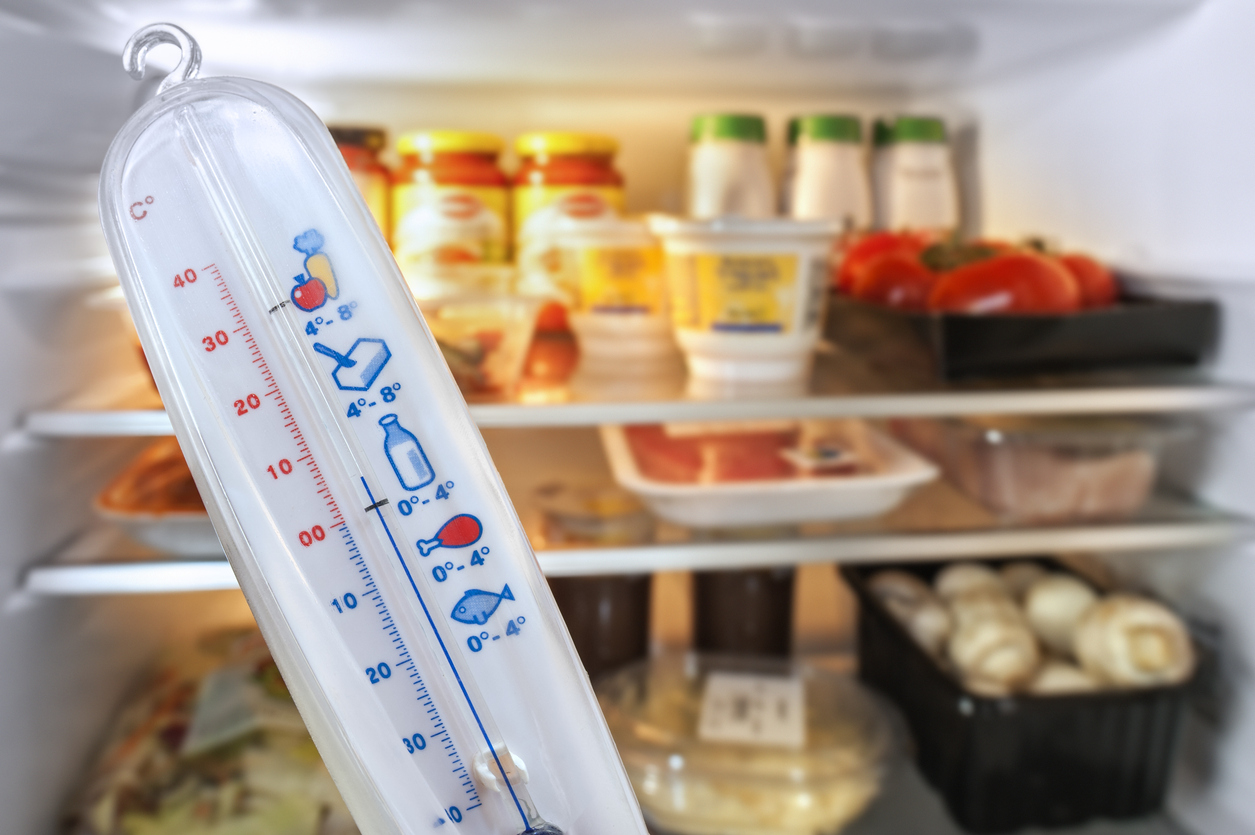Thermometer in front of open refrigerator filled with food in kitchen