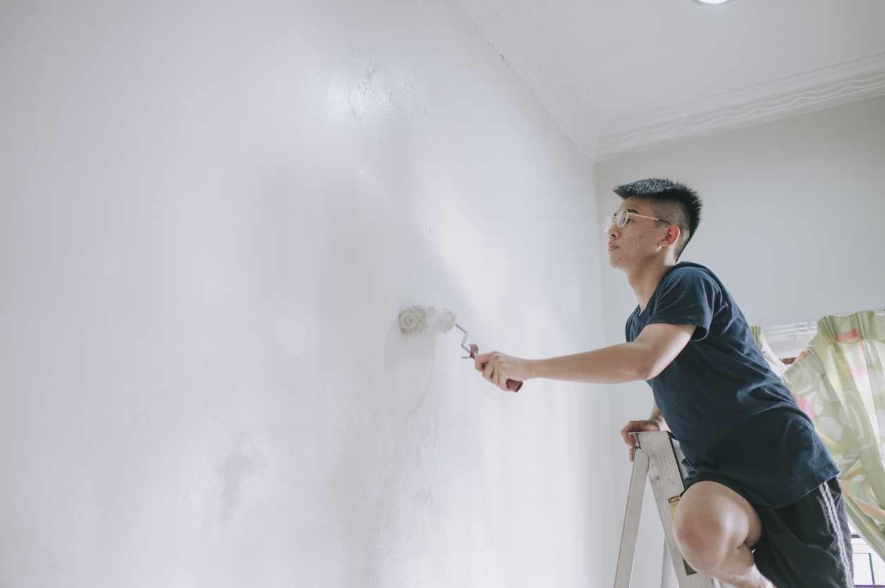 An asian teenage boy painting his bedroom, apartment renovation during sunset