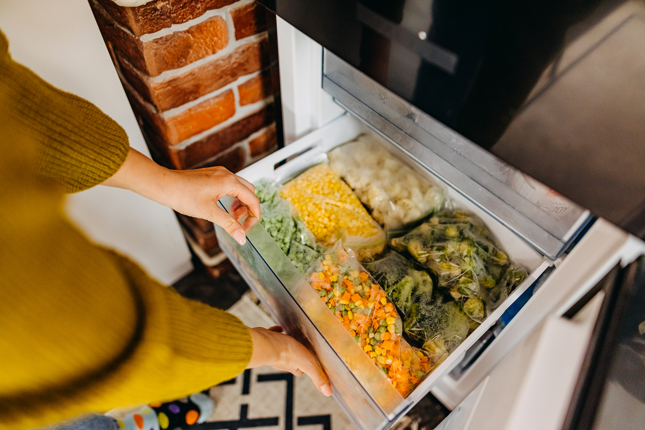 woman opening freezer full of vegetables