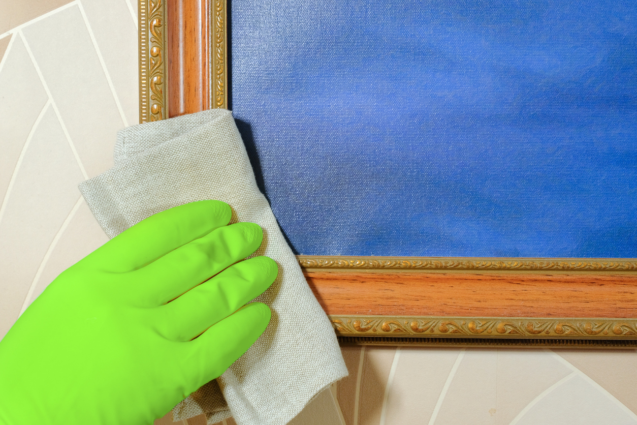 A hand in a rubber glove wipes dust from the picture. Cleaning service.