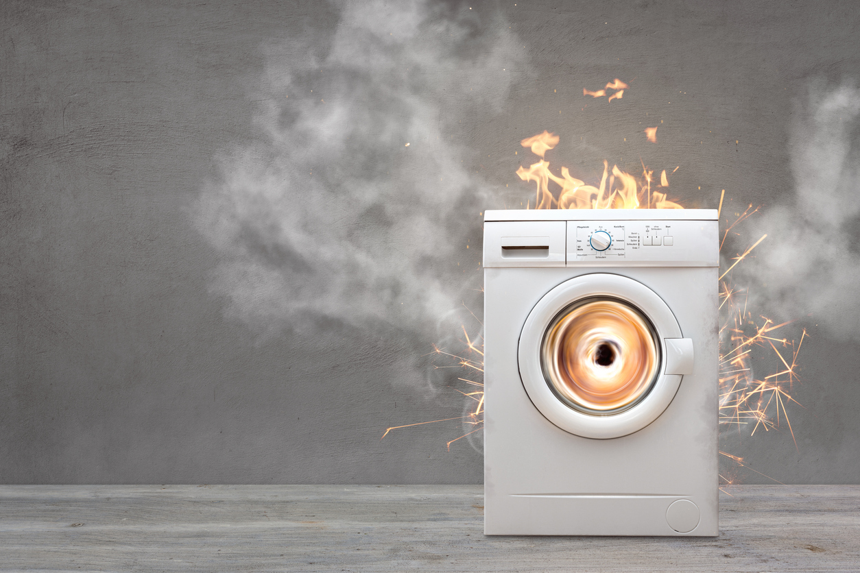 white washer dryer in grey empty room overheating with sparks and flames