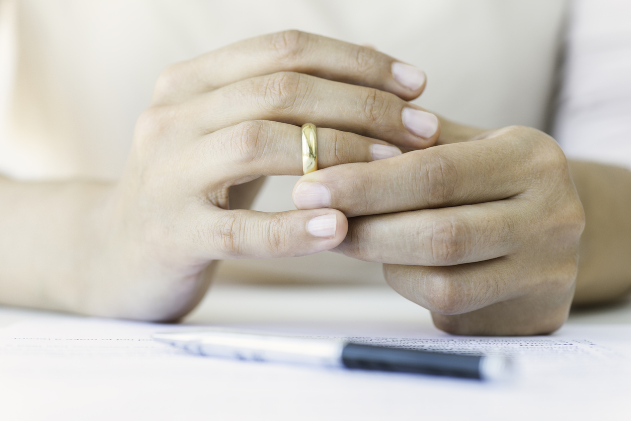 close up on woman's hands removing wedding ring with divorce papers and pen on table