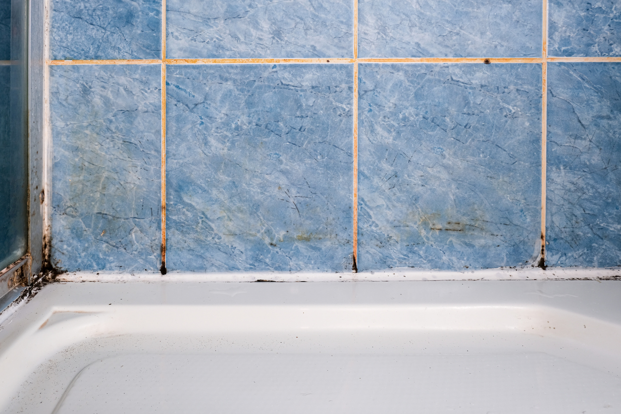 close up on blue tiled wall above bathtub in bathroom with dirty grout and mold