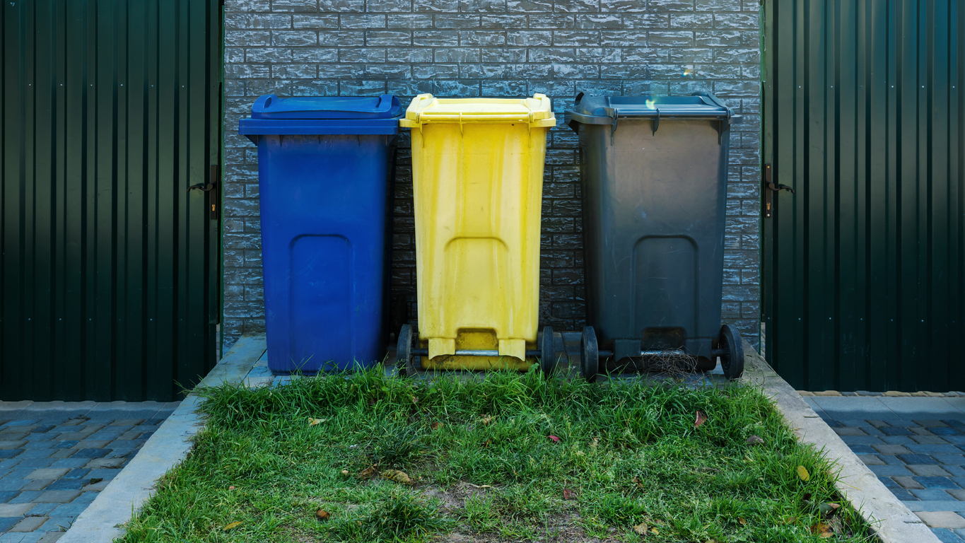 Blue yellow and grey plastic trash bins stands in row on backyard