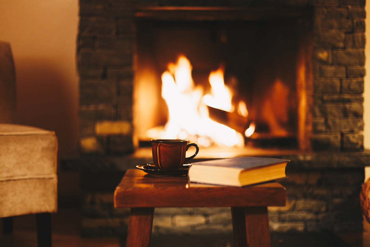 stool with mug and book in front of warm open flame of fireplace in cozy living room