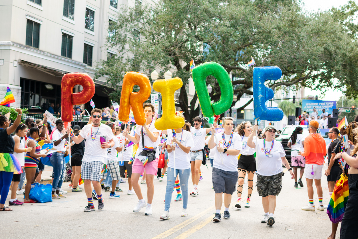 Orlando, Florida, USA, October 15, 2022. Group of members of the LGBTIQIA+ community And Allied Employees of Harmony Healthcare Orlando, with colorful Pride Sign in the Come Out With Pride Orlando parade 2022, on the E Central Blvd street.