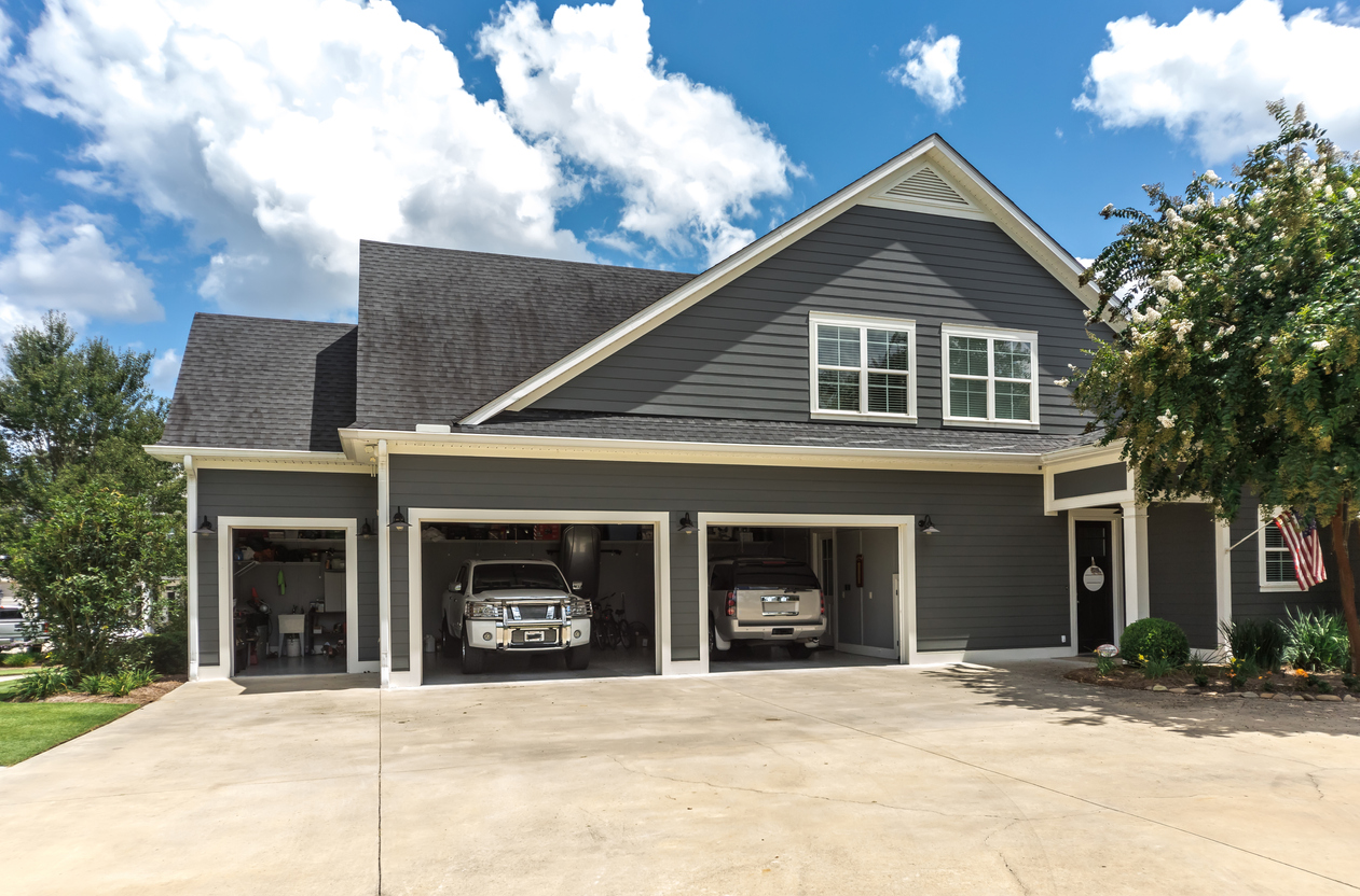 large grey house with driveway and two cars parked in open garage doors