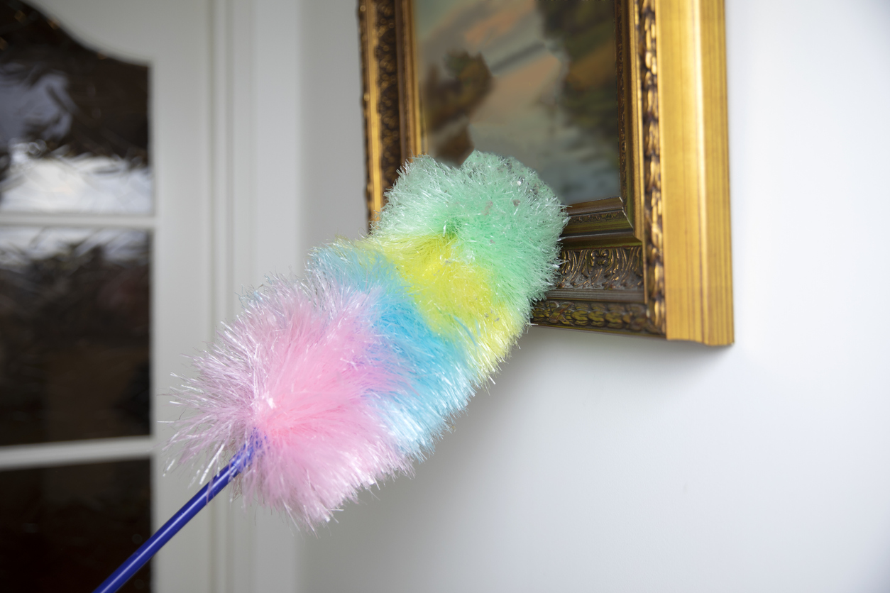Colorful feather duster wiping the dust from oil painting in modern white home, Cleaning concept. Dust on vintage painting close up