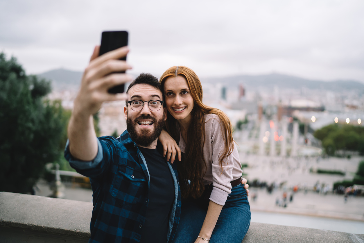 couple poses for selfie while on vacation in front of city landscape