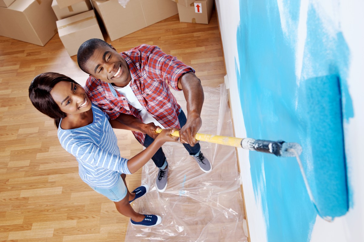 high overhead view of young black couple painting wall with roller in new house