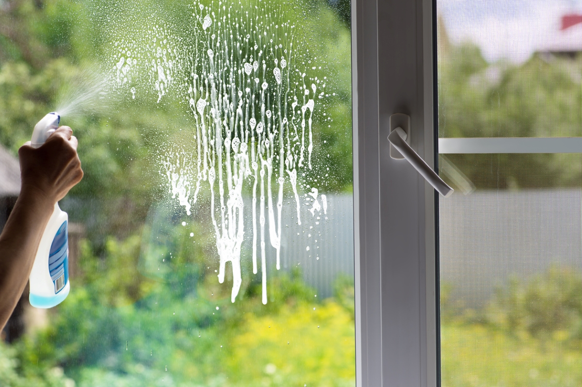 Person spraying cleaning solution on window
