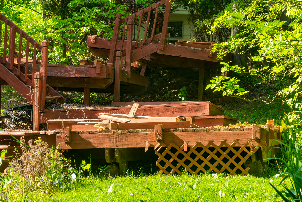 broken-deck-stairs-with-rotten-wood-and-crooked-railings-in-front-of-green-shrubbery