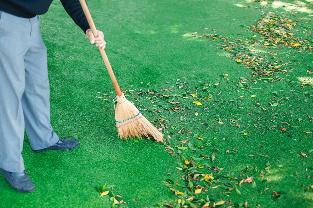Person using broom to sweep turf lawn