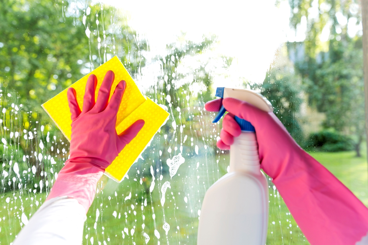 Gloved hands cleaning window with yellow towel