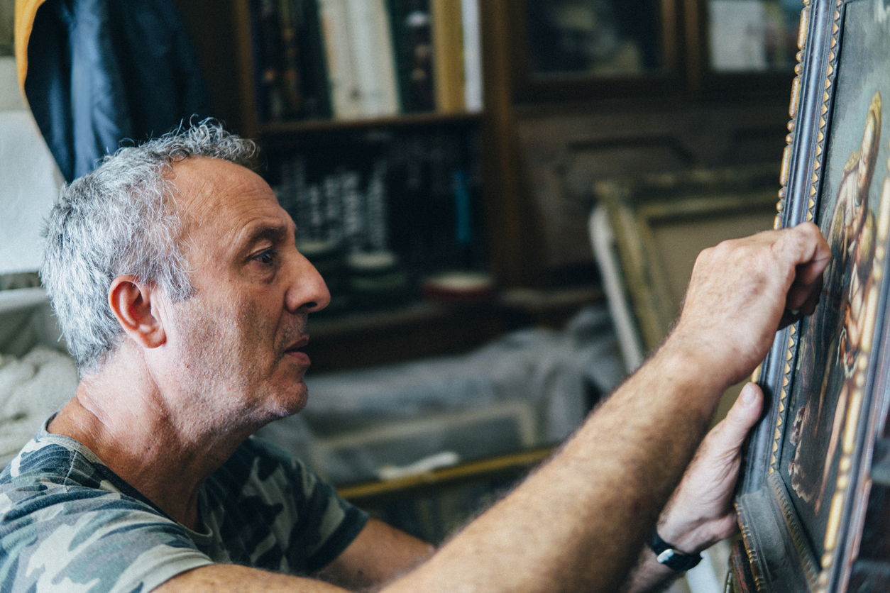 A senior restorer repairing an ancient canvas in his workshop