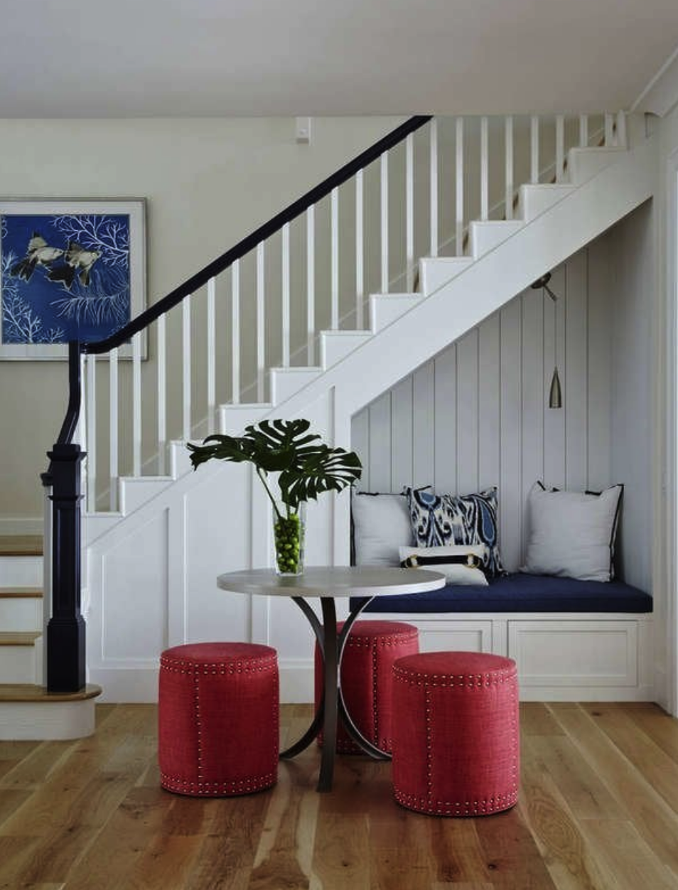 entryway view of staircase with cushioned bench inside nook behind round table with cylindrical red stools