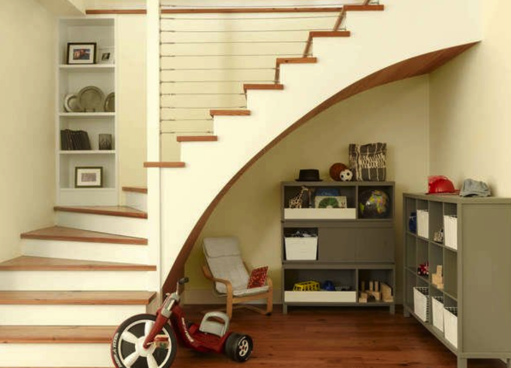 staircase with curved bottom with small children's play space underneath with chair and toy shelves