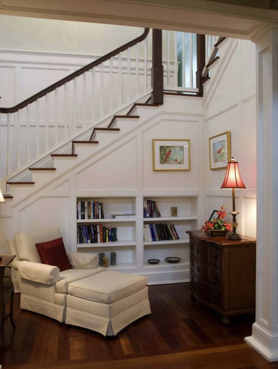 stately living room with white chair and white ottoman and white staircase with bookcase built in underneath