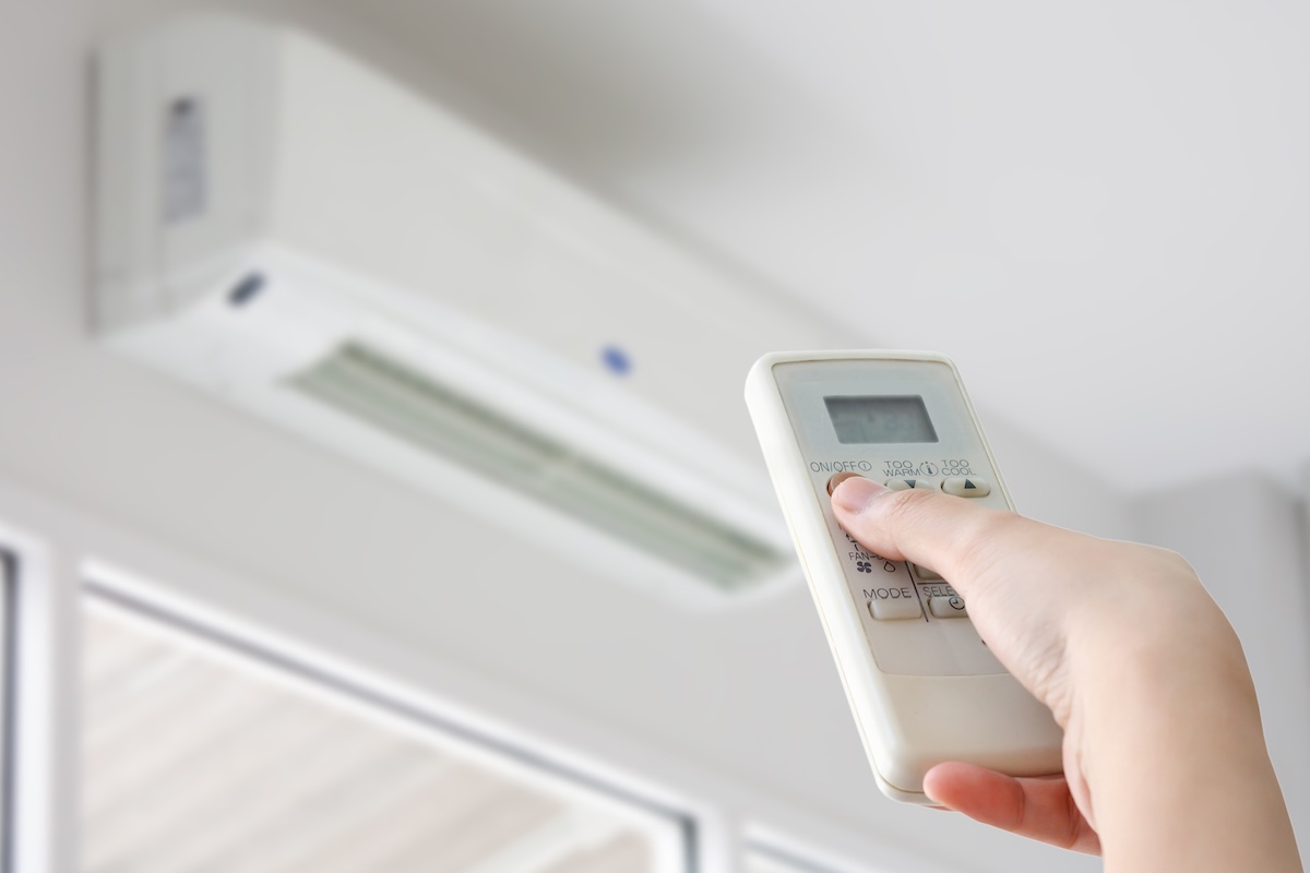 Hand with remote control directed at a mini-split air conditioner.