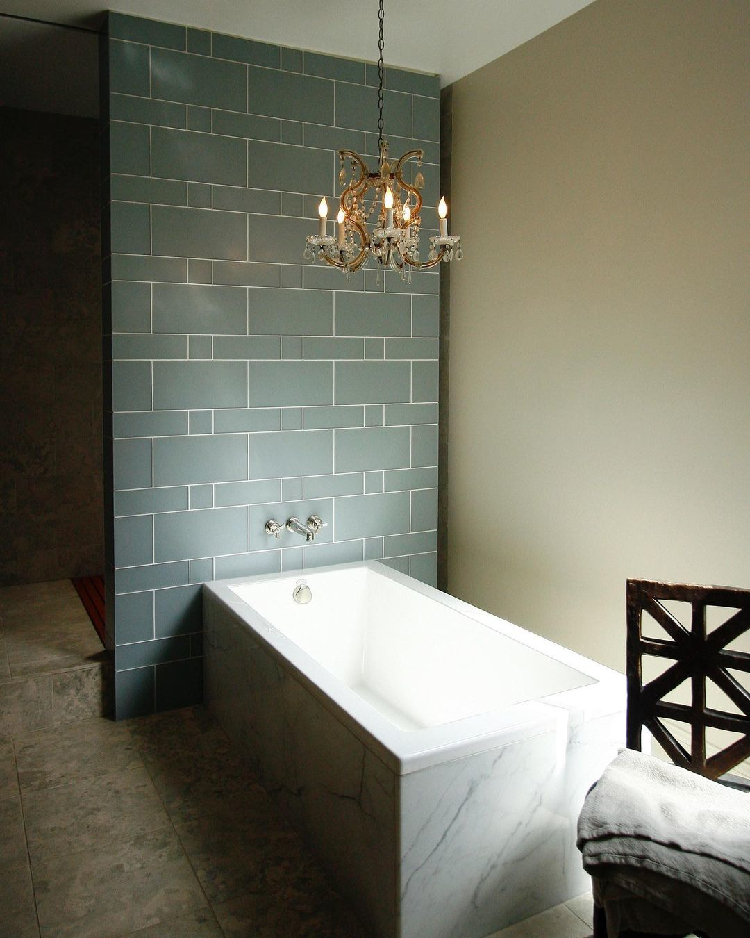 Small bathroom with a green tile accent wall and a small LED chandelier hanging over a drop-in bathtub