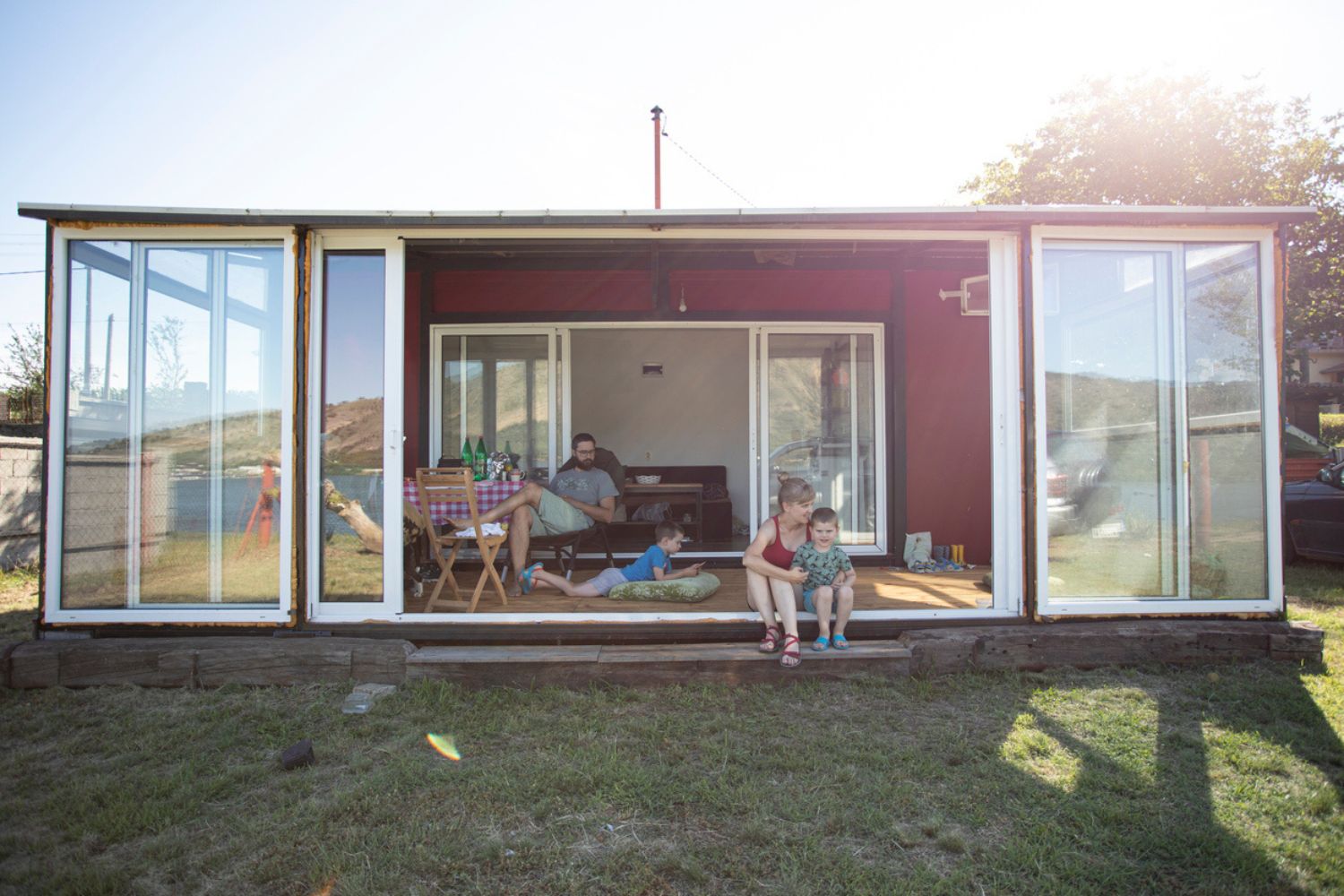 A family sites outside a container home on a sunny day.