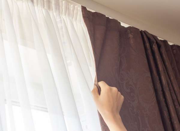 Woman closing blackout curtain over lighter curtain