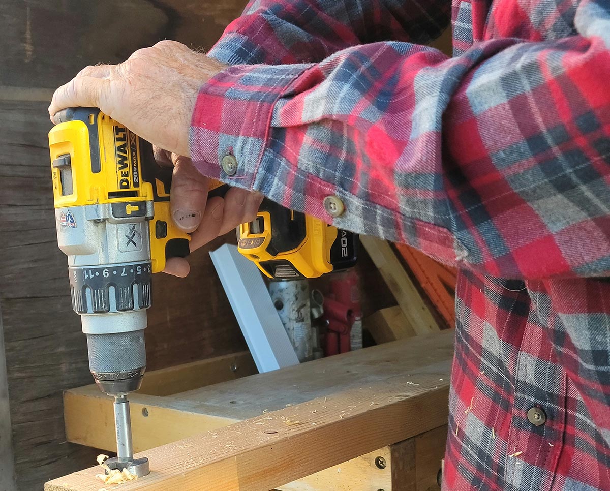 A person using a DeWalt tool powered by a DeWalt PowerStack battery to bore a hole through a piece of wood