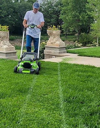 A person using the Greenworks Pro 60V 21-Inch Battery Lawn Mower to mow a bright green lawn