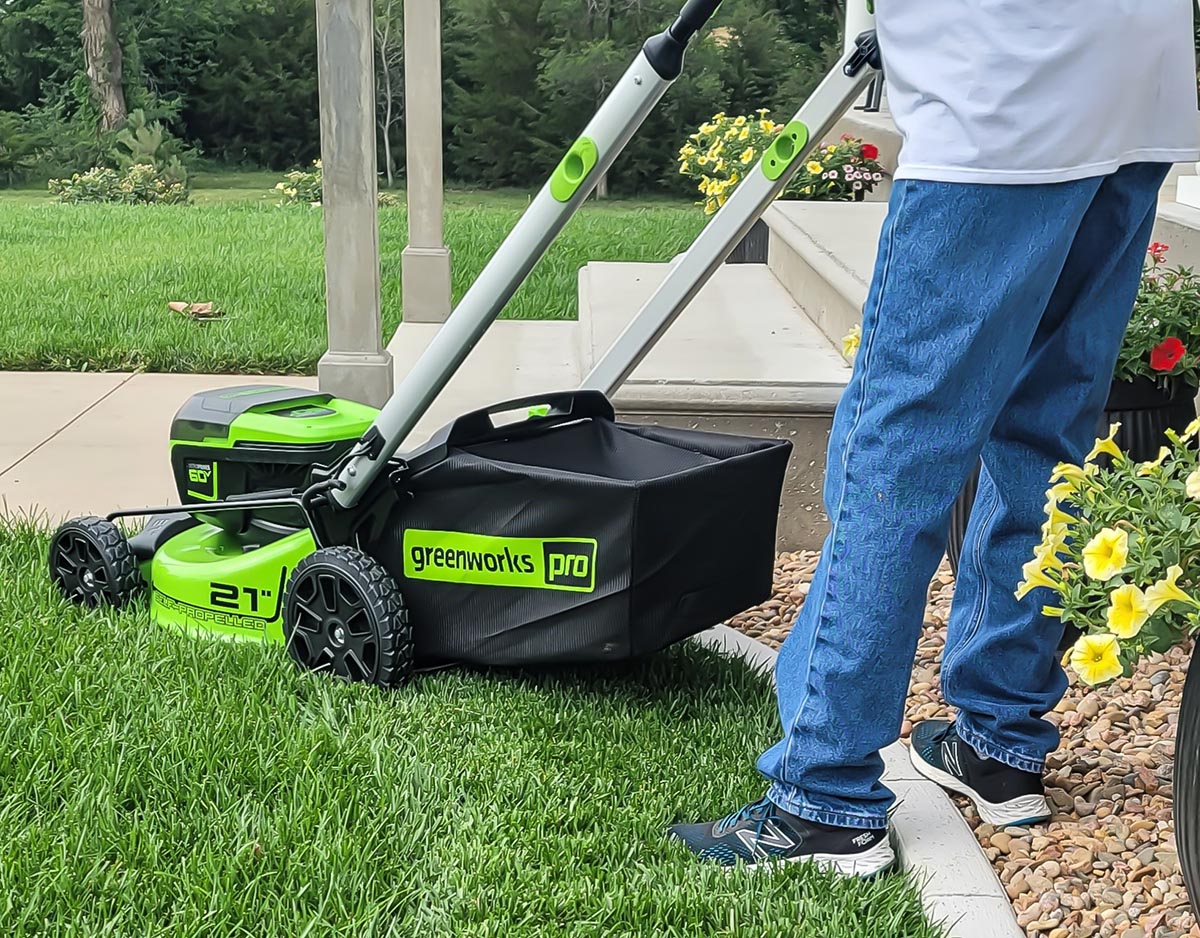 A person using the Greenworks Pro 60V 21-Inch Battery Lawn Mower to mow a bright green lawn