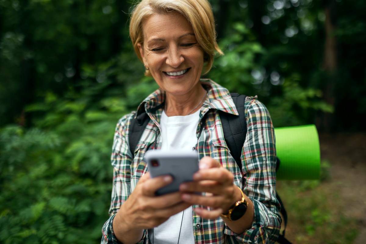 Mature female hiker smiling while looking at her phone on a trail
