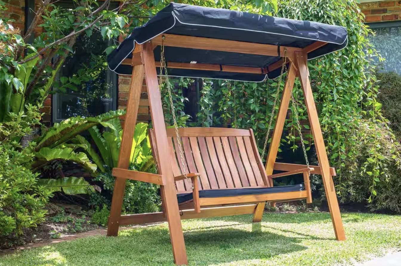 Swinging garden seat with black awning sitting in a yard.