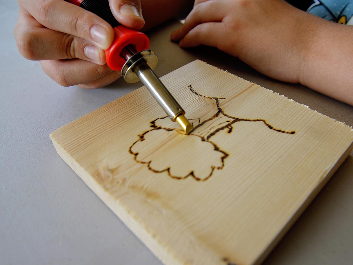 Person using TRUArt Stage 1 Wood-Burning Tool to draw tree on wood