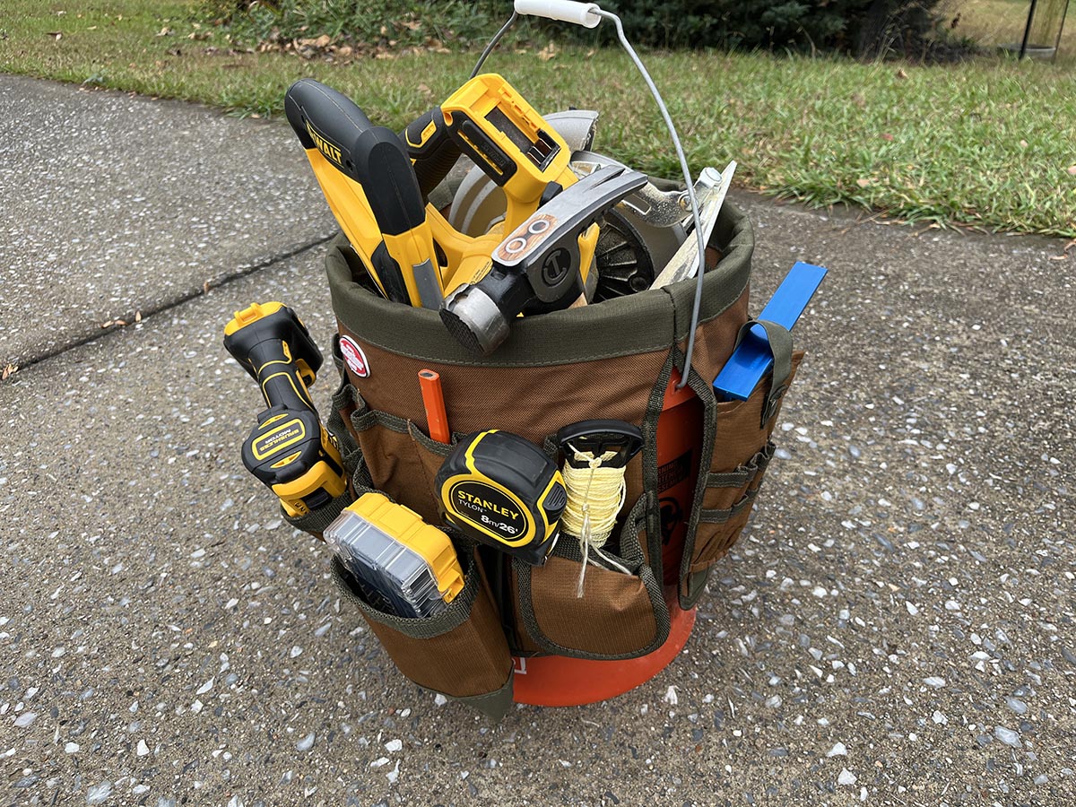 Bucket Boss 5-gallon canvas tool holder filled with hand and power tools, sitting on concrete driveway