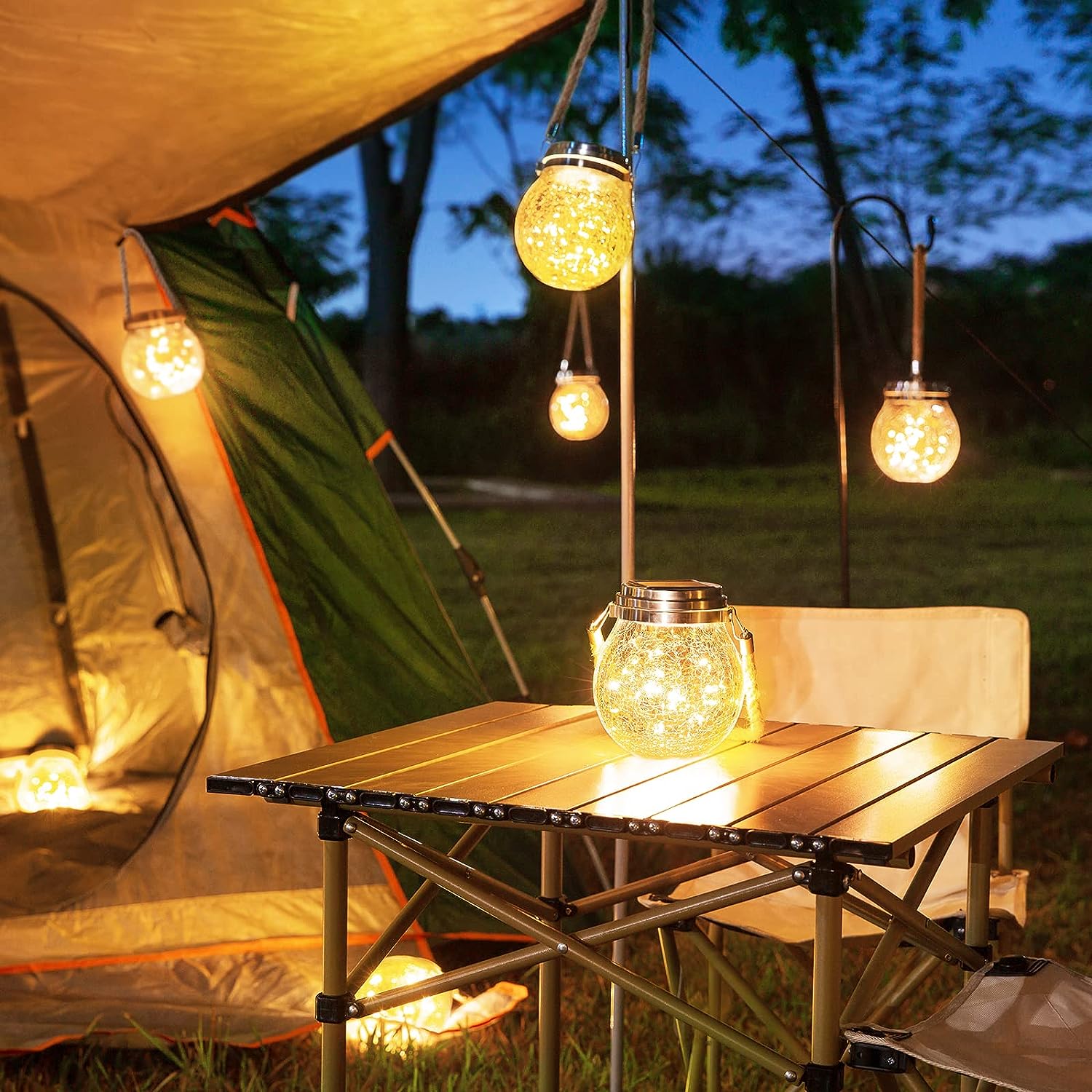 close view of camp site with tent and covered table lit by warm string lanterns