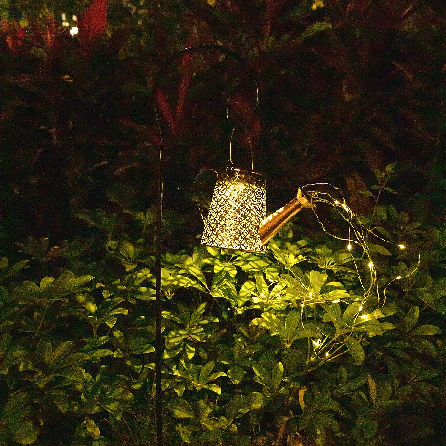 night shot of hook light shaped like a watering can with string lights coming out of spout