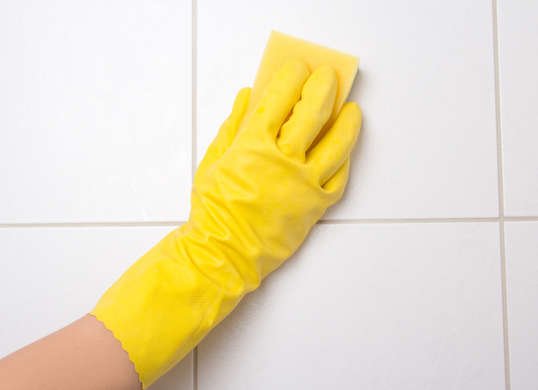Hand in yellow glove scrubbing wall with sponge