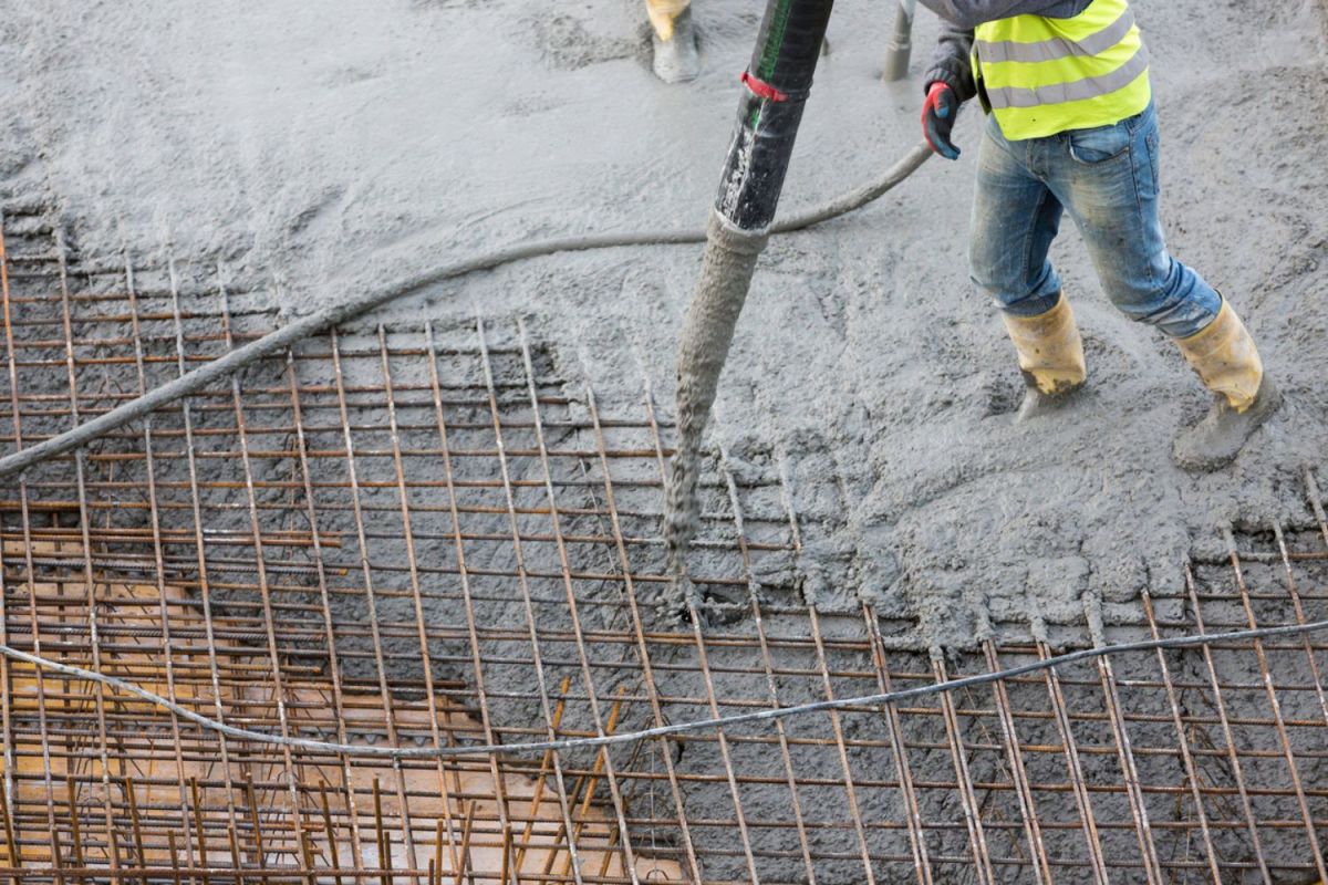 A worker pouring concrete while wearing the best work boots for concrete