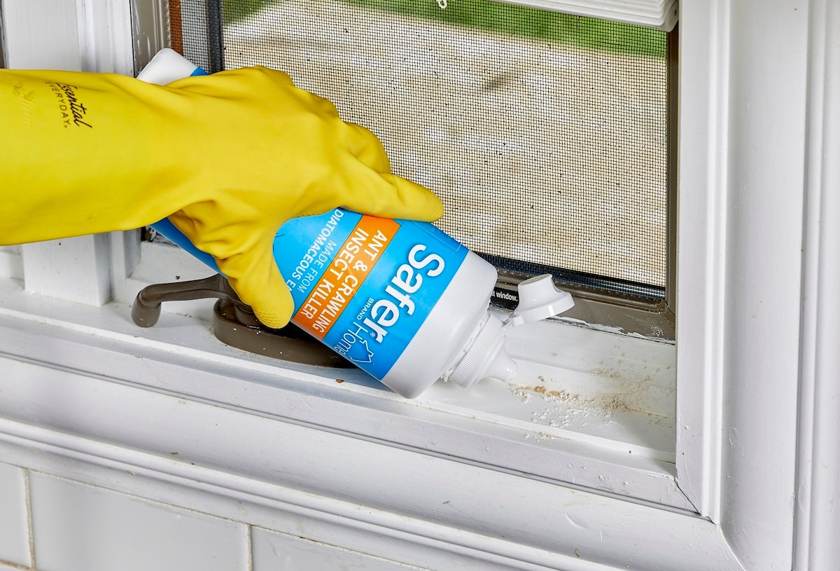 Woman wearing yellow rubber glove puts diatomatceous earth along a window sill.